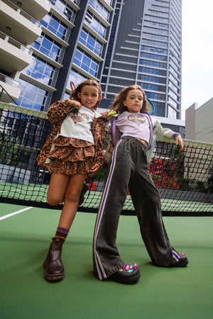 Two girls on a city rooftop court, one in Untamed leopard jacket and ruffle skirt, one in black Slay Queen wide leg pants – Little Baddie