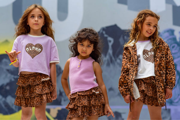 Three girls in Little Baddie leopard ruffle skirts with ALPHA heart tees and Untamed leopard windbreaker